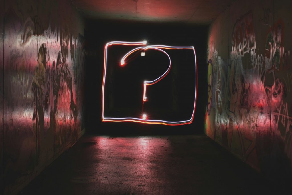 Abstract neon question mark in a dark underground tunnel with graphiti